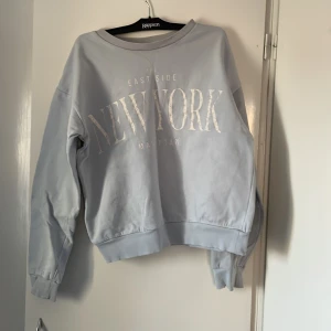 Ljusgrå sweatshirt från Kappahl - Säljer en ljusgrå sweatshirt från Kappahl med texten 'New York' tryckt på framsidan. Tröjan har långa ärmar och en rund halsringning. Perfekt för en avslappnad stil. Hör av dig vid intresse!