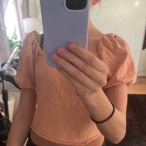 Rosa topp - Säljer en söt rosa topp med puffiga korta ärmar och smockdetaljer. Toppen är croppad och har en elastisk passform som gör den bekväm att bära.