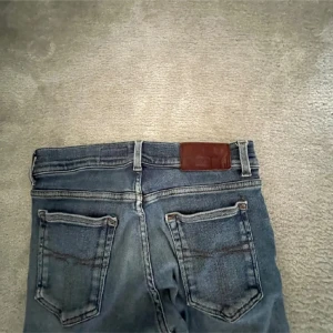 Tiger of Sweden jeans  - Snygga blå jeans med en klassisk femficksdesign och en läderdetalj vid midjan. De har en smal passform och är perfekta för en avslappnad stil. Jeansen har en lätt tvättad look som ger dem en cool vibe.