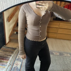 Beige ribbad kofta med knappar - Säljer en beige ribbad kofta med v-ringning och knappar framtill. Tröjan har långa ärmar och en croppad passform, perfekt för en stilren look.