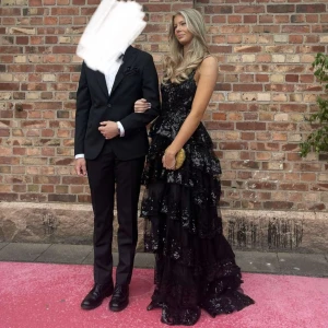 Svart glittrig balklänning  - Intressekoll på min balklänning. Den är svart med glittriga detaljer och volanger, plus en slits vid ena benet. Hade klänningen på min bal så enbart använd en gång. Skriv för mer information och bilder. Pris är diskuterbart💕 Köpt för 3500kr