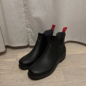 Svarta låga gummistövlar från McKinley - Snygga svarta boots från McKinley med röd dragflik. Perfekta för höst och vinter. Tillverkade i syntetmaterial med elastiska paneler för enkel påtagning. Använda ett par gånger