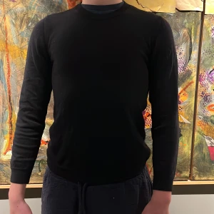 Merinoull  - Säljer en stilren svart långärmad tröja. Perfekt för en minimalistisk look. Tröjan har en klassisk passform och är gjord i ett mjukt material som känns skönt mot huden. Passar till många olika outfits och tillfällen.