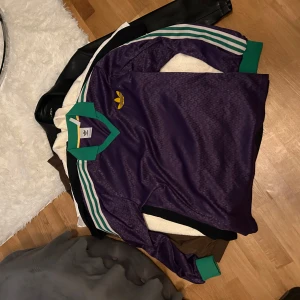 Lila långärmad tröja från Adidas - Säljer en cool lila tröja från Adidas med gröna och vita detaljer. Tröjan har långa ärmar och en klassisk Adidas-logga på bröstet. Perfekt för en sportig look eller avslappnad stil.