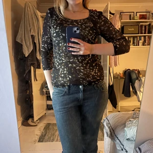 Söt topp med trekvarts ärm - Säljer en svart topp med lövmönster i brunt och vitt. Toppen har en dekorativ kant runt halsringningen som ger en extra touch. Perfekt för att göra vardagen lite roligare. 