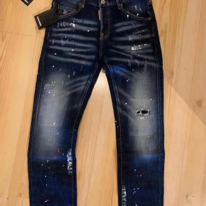 Mörkblå jeans från Dsquared2 - Snygga mörkblå jeans från Dsquared2 med coola slitningar och färgstänk. De har en klassisk femficksdesign och knappgylf. Perfekta för en trendig look.