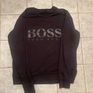 Svart tröja från Hugo Boss - Säljer en  svart tröja från Hugo Boss med en logga på framsidan. Tröjan har en normal passform och långa ärmar, har använda ett par gånger. Ny pris runt 1299kr. Passa på att köp🤩.