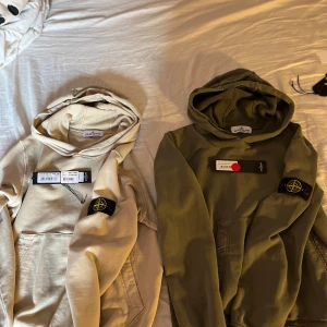 Beige och grön hoodie från Stone Island - Två stilrena hoodies från Stone Island i beige och grön färg. Båda har den ikoniska logotypen på ärmen och en klassisk huva. Perfekta för en avslappnad look.Köpt på NK i Göteborg för 1799 styck