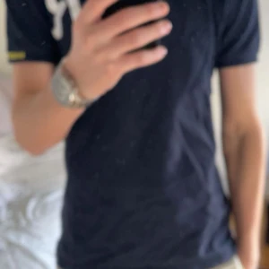 Mörkblå pikétröja från Replay - Säljer en snygg mörkblå pikétröja från Replay med ett stort 'R' broderat på bröstet. Tröjan har korta ärmar och en klassisk krage med knappar. Tröjan har används ganska mycket men det finns inga stora synliga defekter. Pris kan diskuteras.