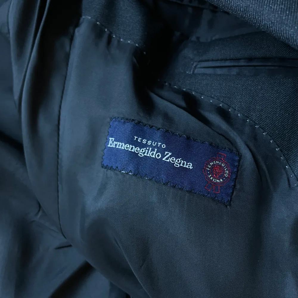 Elegant mörkgrå kostym från Ermenegildo Zegna. Kavajen har klassisk design med knappar och byxorna har en stilren passform. Perfekt för formella tillfällen. Mått kavaj: Längd baktill från slutet av krage och ner: 70cm. Axel till axel: 44 cm. Armhåla till armhåla: 42cm. Ärm 60 cm. Mått byxa: Längd: 93 cm. Insida ben: 71 cm. Öppning ben 19 cm. Midja: 40 cm. (Mått tagna med plagget liggandes platt). Puvut & Bleiserit.