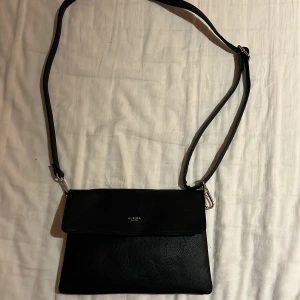 Svart axelväska från Ulrika - Snygg svart axelväska från Ulrika i skinn. Perfekt för att bära med sig det viktigaste. Väskan har en justerbar axelrem och en stilren design som passar till många tillfällen.