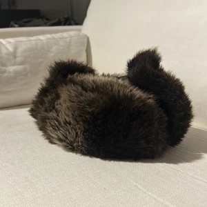 Brun pälsmössa från H&M - Säljer en mysig brun pälsmössa från H&M. Mössan är tillverkad i imitationspäls och har en mjuk insida för extra komfort. Perfekt för kalla vinterdagar.