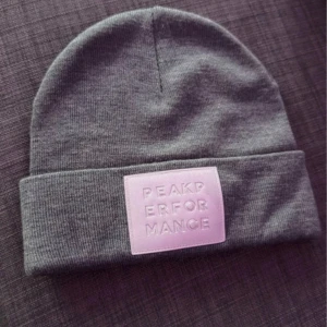 Grå mössa från Peak Performance - Snygg grå mössa från Peak Performance med en uppvikt kant och ett stilrent märke framtill. Perfekt för kyliga dagar och ger en sportig look. Tillverkad i mjukt material för extra komfort.