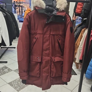 Vinröd Yatesy parkajacka från Nobis - Säljer en stilren vinröd parkajacka från Nobis med pälsdetaljer på huvan. Jackan har flera praktiska fickor med knappar och en broderad logga på ärmen. Perfekt för kyliga dagar med sin långa passform och skyddande design.