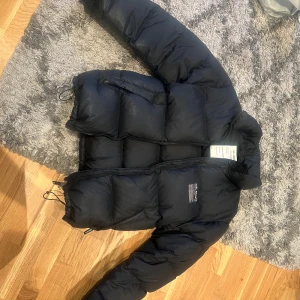 Svart dunjacka från Axel Arigato - Säljer en svart pufferjacka från Axel Arigato. Jackan är tillverkad av 100% återvunnen polyester och har en klassisk pufferdesign med dragkedja framtill. Perfekt för kyliga dagar.