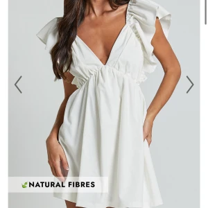 Vit klänning med volangdetaljer - Snygg vit klänning med djup v-ringning och volangdetaljer på axlarna. Klänningen har en öppen rygg med knytning. Perfekt till studenten. Endast testad! Lappar kvar!🤍