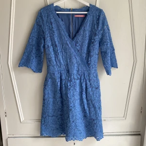 Himmelsblå spetsklänning från Pernilla Wahlgren - Ljuvligt himmelsblå spetsklänning från Pernilla Wahlgren med omlott-design och trekvartsärmar. Klänningen har en dragkedja bak med en söt hjärtformad detalj. Sköna fickor i sidorna. Längd 94 cm. Använd en gång. 