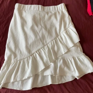 Vit kjol med volang från Nelly stl S - Snygg vit kjol med volangdetaljer i stl S. Perfekt för sommarens alla tillfällen. Har endast använt på min student. Köparen betalar frakt☺️