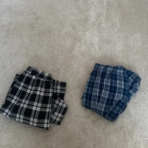 Två par rutiga byxor/pyjamosbyxor  - Kan säljas sepperata. Säljer två par rutiga byxor, ett par i svartvitt och ett i blåvitt. Båda har elastisk midja för extra komfort. Perfekta för en avslappnad stil.