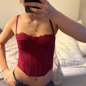 Röd korsett med spetsdetaljer - Snygg röd korsett med spetsdetaljer och justerbara axelband. Perfekt för en elegant look. Den har en vacker struktur och ger en smickrande passform. Från shein. Storlek xs. 3 spännen där bak. 