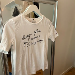 Vit t-shirt från Tommy Hilfiger - Säljer en vit t-shirt från Tommy Hilfiger med texten 'Always follow your dreams' tryckt på framsidan. T-shirten har korta ärmar och en klassisk rund halsringning. Perfekt för en avslappnad stil.