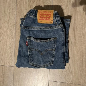 Levi's jeans i klassisk blå denim - Säljer ett par klassiska Levi's jeans i blå denim. De har en rak passform och är tillverkade i slitstarkt jeanstyg. Perfekta för en avslappnad stil. Levi's ikoniska lädermärke syns tydligt på baksidan.