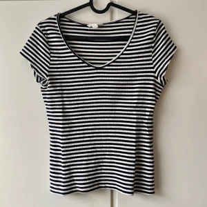Randig kortärmad topp - Säljer en snygg randig topp i svart och vit med korta ärmar och v-ringning. Perfekt för både vardag och festliga tillfällen. Toppen är i bra skick och har en skön passform.