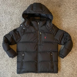 Svart dunjacka från Ralph lauren - Säljer en svart dunjacka från Polo Ralph Lauren i  bra skick kolla senare bilder för små defekter. Jackan har en praktisk huva och dragkedja framtill. Perfekt för kalla vinterdagar. Den har långa ärmar och två fickor med dragkedja för säker förvaring. Storleken är även L ungdom motsvara xs