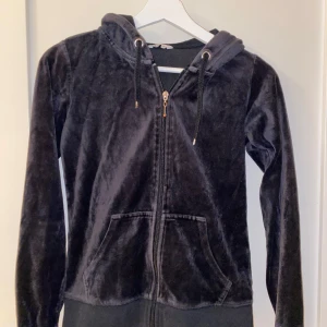 Svart hoodie i sammet - Mysig svart hoodie i sammet med dragkedja och huva i storlek XS. Perfekt för kyliga dagar när du vill vara både bekväm och stilren. Den har långa ärmar och en skön passform. Ett måste i garderoben för alla som älskar mjuka material. Den är i jättebra skick och väldigt skön! Pris kan diskuteras.
