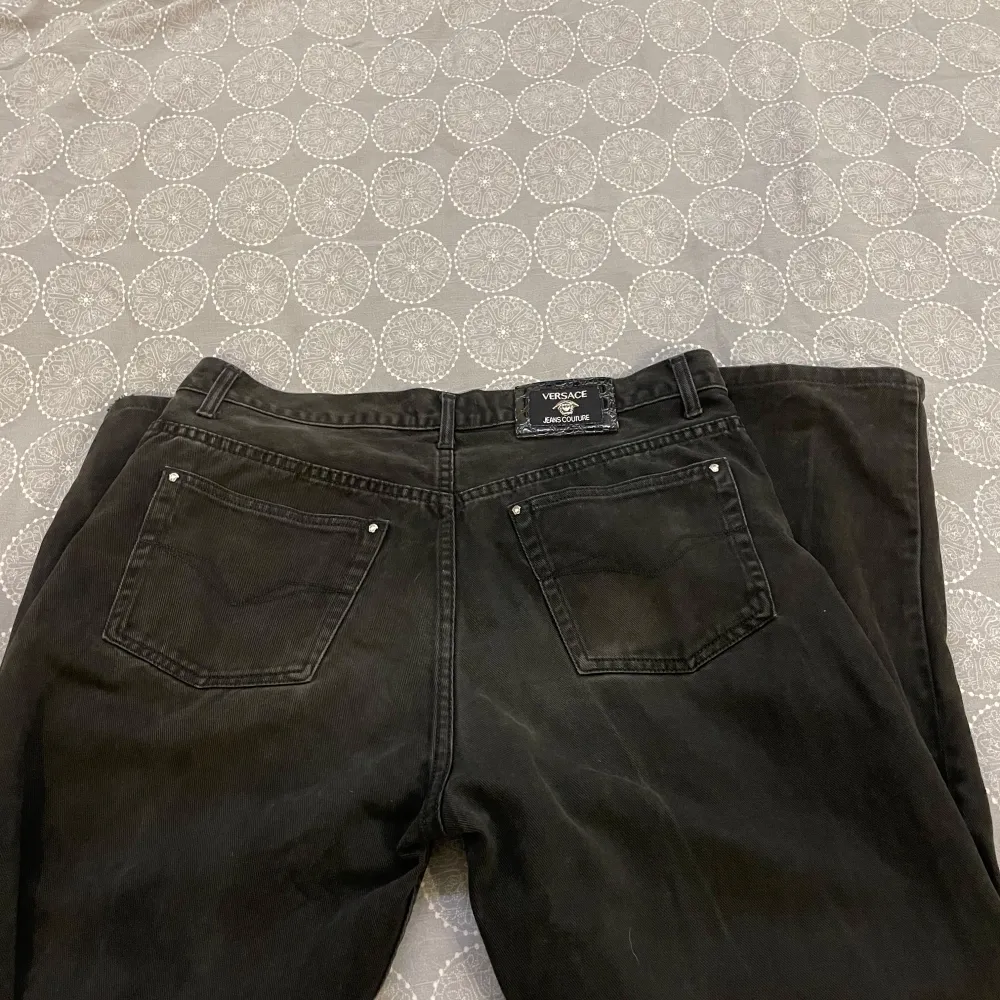 Säljer ett par snygga svarta jeans från Versace Jeans Couture. De har en klassisk femficksdesign och en stilren look med märkets logga på knappen och bakfickan. Perfekta för både vardag och fest!. Farkut & Housut.