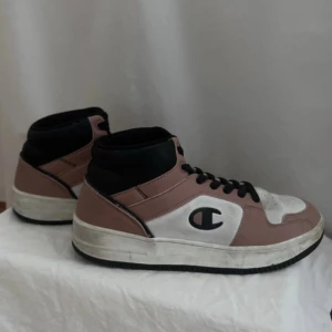 Champion sneakers i rosa och vit - Säljer ett par Champion sneakers i rosa och vit med svart snörning och detaljer. Skorna har en hög modell med bekväm passform. De är i bra skick med lite slitage på sulan, går att rengöra lätt så ser de ut som nya och fräscha! 