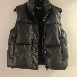 Svart dunväst från Zara - Säljer en svart dunväst från Zara i mycket bra skick. Västen har en stilren design med knappar och dragkedja framtill.
