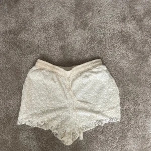 Vita spets shorts från Lindex - Säljer ett par superfina vita spets shorts från Lindex i storlek M. De har ett blommigt mönster och är små i storleken. Använd endast 1 gång.
