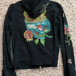 Säljer en cool svart hoodie från Ed Hardy med färgglada broderade motiv av en dödskalle med krona och blommor. Den har dragkedja fram och långa ärmar med mönster. Perfekt för en unik och stilfull look! Skulle själv säga att den är lite 2000s vibe. Xl I barnstorlek som motsvarar s I vuxen storlek. Det är bara att skriva om du har några frågor 💕💕