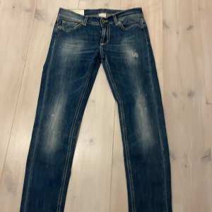 Blå jeans från Dondup - Säljer ett par snygga blå jeans från Dondup i modellen Archie. De har en klassisk femficksdesign och är tillverkade i Italien. Jeansen har en sliten look med ljusare partier och är i bra skick.