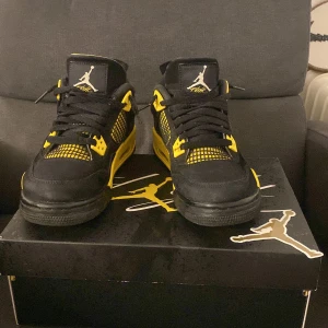Nike Air Jordan 4 Retro Thunder (2023)(gs) - Säljer ett par Nike Air Jordan 4 Retro Thunder från 2023 i svart och gul färg. Skorna är i nytt skick och har den klassiska Jumpman-loggan på hälen. Perfekta för både samlare och sneakerheads som vill ha något unikt i sin garderob.