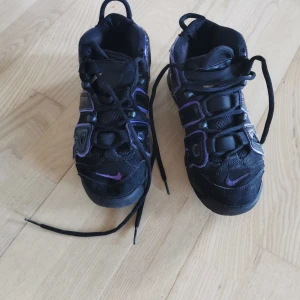 Nike air uptempo, Svarta sneakers med lila detaljer - Säljer ett par coola svarta Nike air uptempo sneakers med lila detaljer. Skorna har snörning och en robust sula med Nike-loggan. Perfekta för vardagsbruk eller träning. De är i bra skick med lite slitage på sulan.