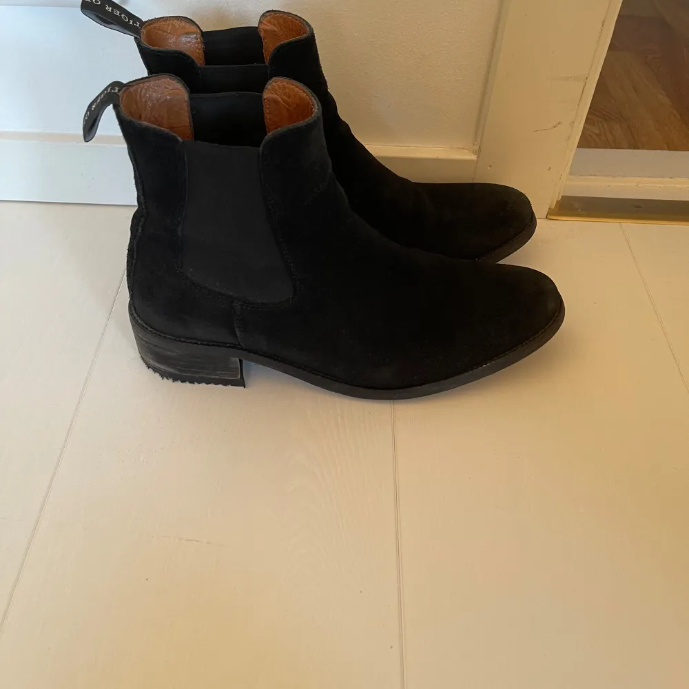 Säljer ett par stilrena svarta Chelsea boots i mocka från Tiger of Sweden. De har en klassisk design med en liten klack. Perfekta för både vardag. Använda men i mycket bra skick. Har adderat en gummisula på klacken hos skomakare. Storlek 40, passar 39-40.. Skor.