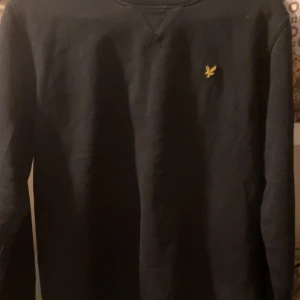 Svart tröja från Lyle & Scott - Säljer en stilren svart tröja från Lyle & Scott i storlek 14/15 år. Tröjan har en liten gul logga på bröstet och är perfekt för både vardag och skola. Den är i bra skick och passar till alla tillfällen. Skön och enkel att matcha med andra plagg!