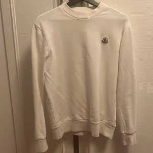 Vit tröja från Moncler - Säljer en stilren vit tröja från Moncler i mycket bra skick. Den har en klassisk design med rund hals och Monclers logga broderad på bröstet. Perfekt för både vardag och fest. Passar till alla säsonger!