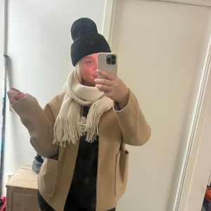 Beige halsduk - Säljer en supermysig créme vit halsduk i stickat material. Perfekt för att hålla sig varm under höst och vinter. Den har en klassisk design med fransar i ändarna!