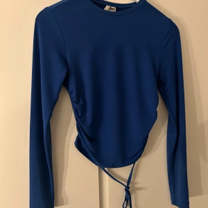 Blå långärmad topp från NLY Trend - Säljer en snygg blå långärmad topp från NLY Trend i storlek XS. Toppen har en cool knytdetalj framtill som ger en unik look. Perfekt för både vardag och fest! 💙