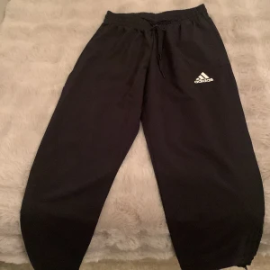 Svarta mjukisbyxor från Adidas - Säljer ett par svarta mjukisbyxor från Adidas i storlek S. De har en elastisk midja med snörning och Adidas-loggan på benet. Perfekta för träning eller som ett par sköna och fina byxor 
