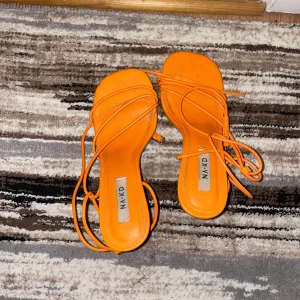 Orange sandaler från NAKD - Snygga orange sandaler från NAKD med knytband som ger en cool look. Perfekta för sommaren och att liva upp vilken outfit som helst. De har en öppen tå och är i syntetmaterial. Perfekta för både vardag och fest!