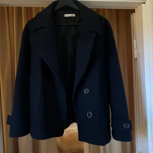 Svart kappa från Design by si  - Säljer en stilren mörkblåa kappa från Design by si i storlek XS/S. Den är gjord av 100% polyester och har en klassisk dubbelknäppning framtill. Perfekt för höst och vår, med långa ärmar och en snygg krage. Passar både till vardags och lite finare tillfällen. 🖤