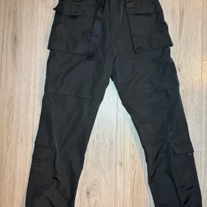 Svarta cargobyxor från Calvin Klein Jeans - Säljer ett par svarta cargobyxor från Calvin Klein Jeans i storlek S. Byxorna har flera praktiska fickor och ett justerbart bälte i midjan. Perfekta för en casual look eller utomhusaktiviteter. Materialet känns slitstarkt och bekvämt. Passar bra till både vardag och äventyr!