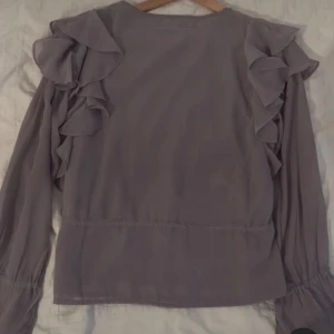 Lila blus med volangdetaljer - Säljer en superfin lila blus från Bik Bok med volangdetaljer på axlarna och ärmarna. Blusen har långa ärmar och en knytning i midjan för en snygg passform. Perfekt för både vardag och fest! 💜