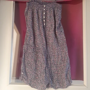 Blommig jumpsuit shorts  - Söt blommig jympsuit i mörkblått med små rosa och vita blommor. Den har knappar framtill och en bekväm passform. Perfekt för vår och sommar! 🌸