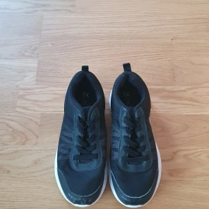 Svarta sneakers med vit sula - Säljer ett par svarta sneakers i mycket bra skick. De har en stilren design med snörning och en vit sula som ger en snygg kontrast. Perfekta för både vardag och träning. Storleken är inte angiven, men de ser ut att passa en normal passform.