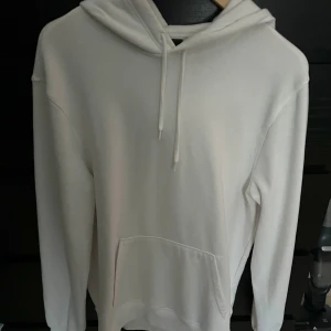 Vit hoodie i bomull - Säljer en stilren vit hoodie i mjukt bomullsmaterial. Den har en klassisk design med långa ärmar och en praktisk magficka. Perfekt för både vardag och mysiga hemmakvällar. Passar till alla säsonger!